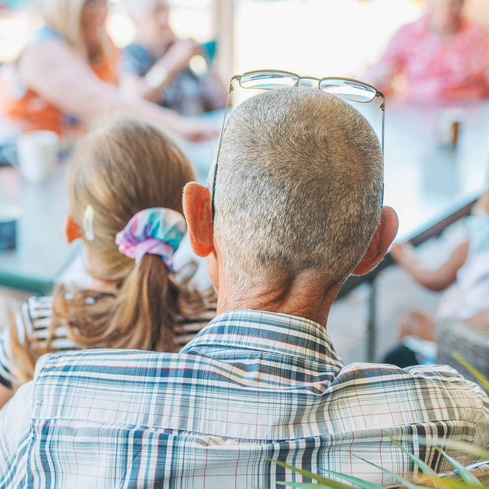 Grandfather carer holding granddaughter on lap while around table with other grandparents